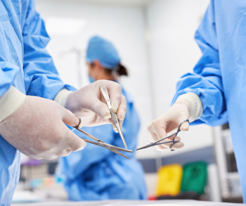 Two pairs of hands wearing surgical gloves and holding surgical tools