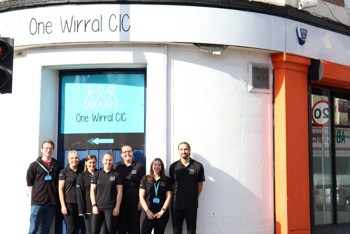 A group of people stood outside of a building. The sign on the building reads "One Wirral CIC"