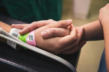 Two hands clasp tightly, one wearing hospital wristbands, suggesting support and care in a medical setting. 