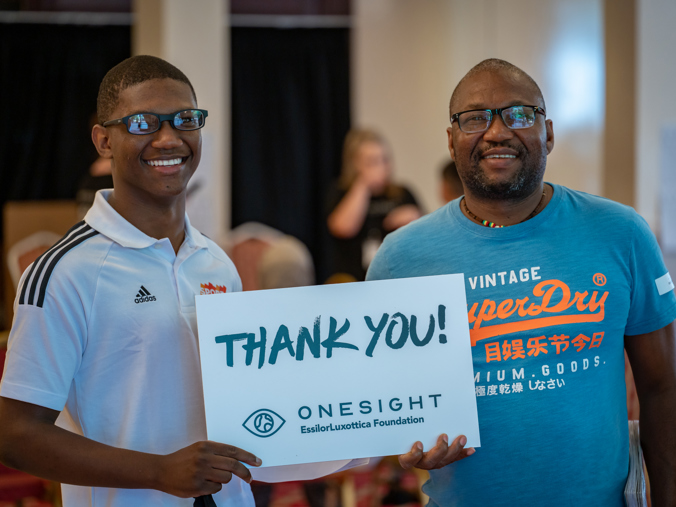 Two men holding the same sign that reads "Thank You! Onesight"