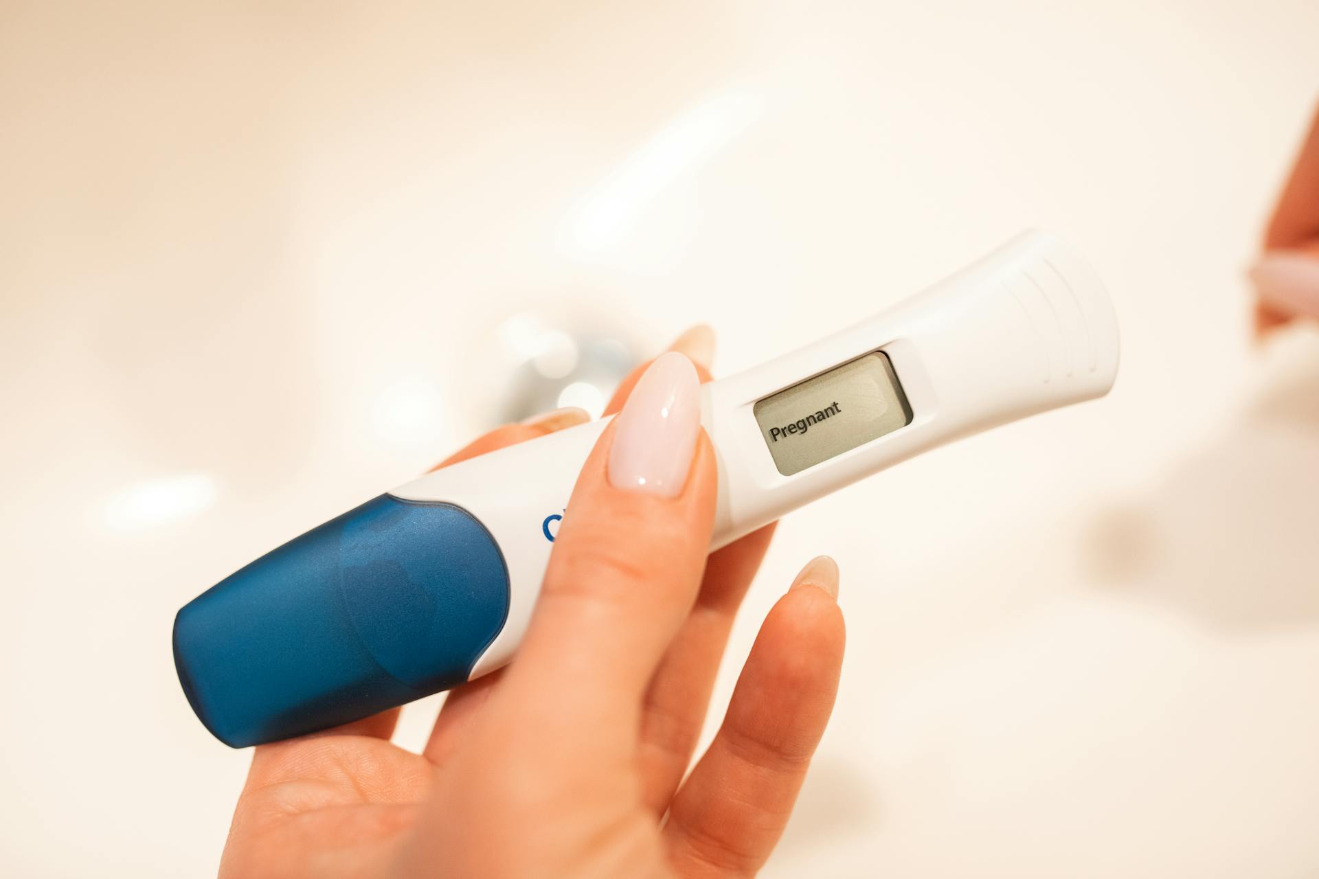 A hand holding a digital pregnancy test showing "Pregnant" on the display. 