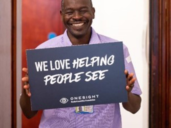 A man holding a sign which says "we love helping people see"