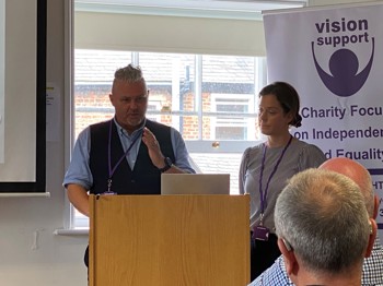 A man and a woman stood behind a podium delivering a presentation