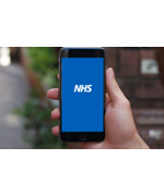 A hand holding a smartphone. The text on the screen reads "NHS"