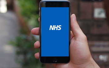 A hand holding a smartphone. The text on the screen reads "NHS"