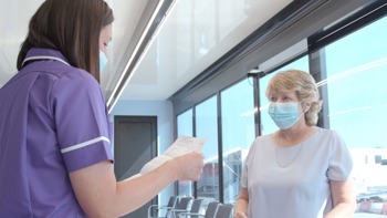 A healthcare professional ready a piece of paper to a women who is wearing a face mask