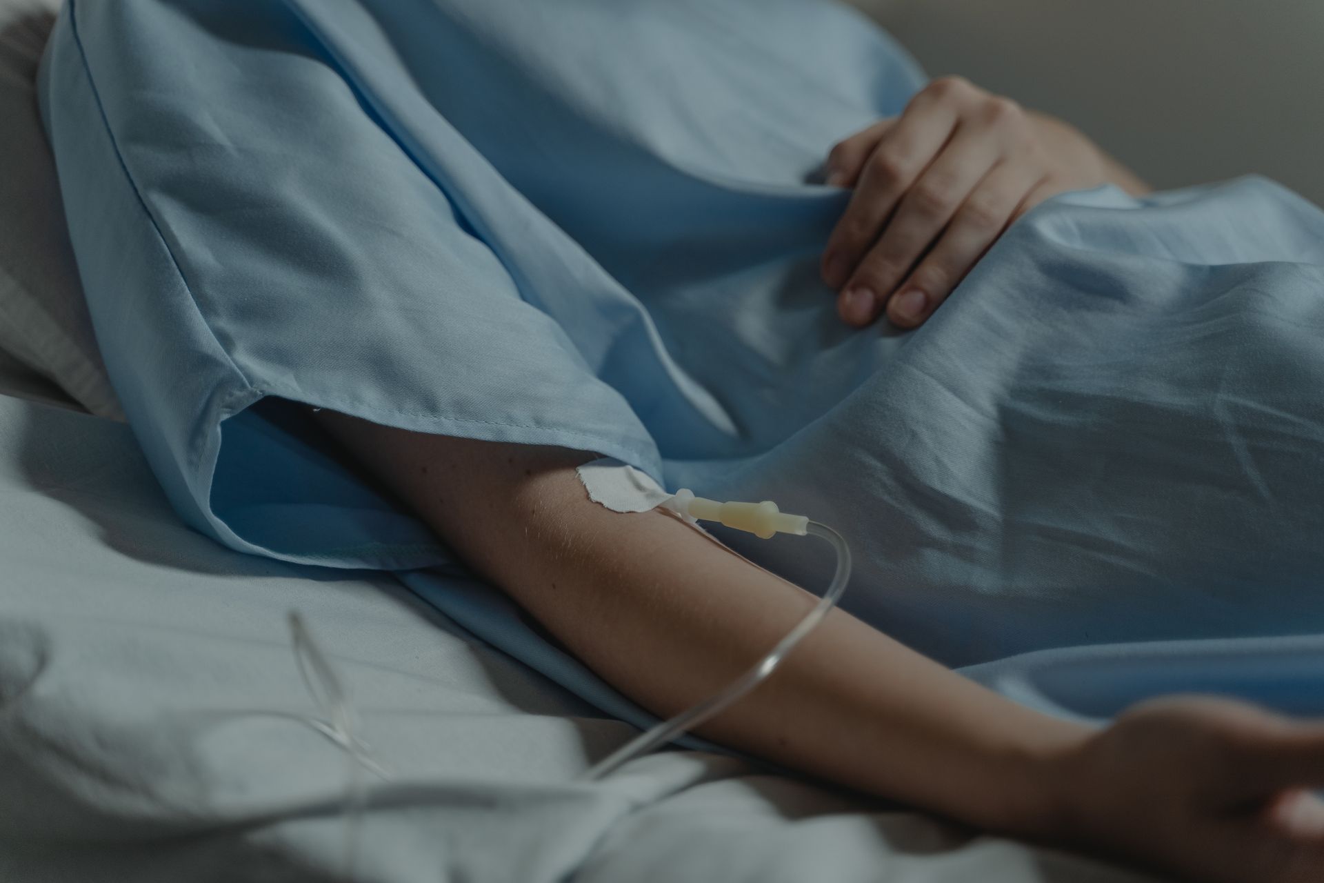 A person in a hospital bed wearing a blue gown with an IV line connected to their arm.