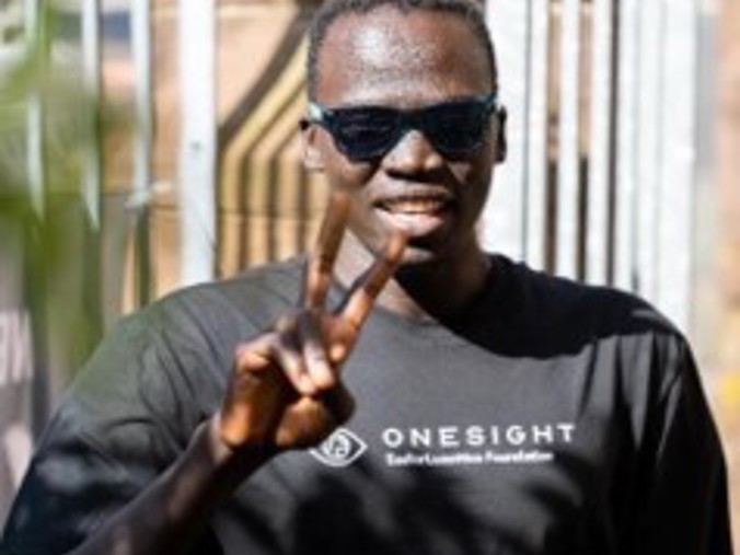 A man wearing sunglasses holding up two fingers in a peace sign, wearing a t-shirt which reads "Onesight"