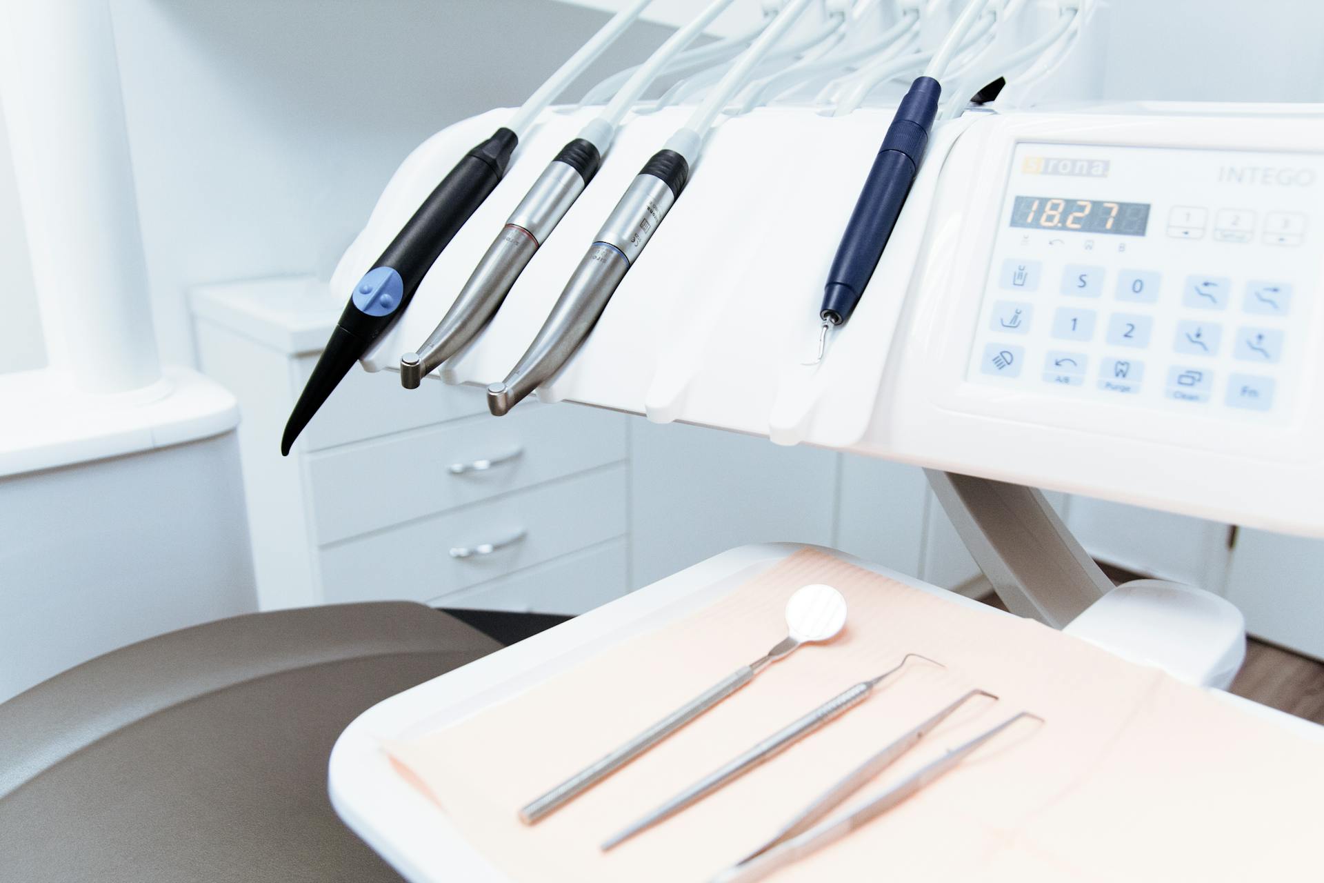 Close-up of a dental workstation featuring dental tools, a digital control panel, and a tray. 