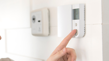 A thermostat on the wall being adjusted to increase the temperature